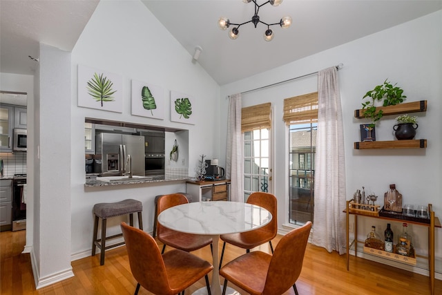 dining space featuring vaulted ceiling, sink, a notable chandelier, and light wood-type flooring