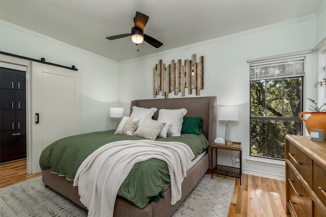 bedroom with multiple windows, ornamental molding, a barn door, and light hardwood / wood-style floors