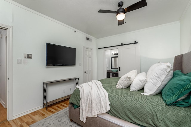 bedroom featuring crown molding, hardwood / wood-style flooring, a barn door, and ceiling fan