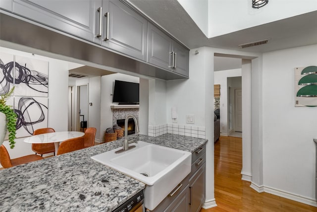 kitchen with light wood-type flooring, light stone countertops, sink, and gray cabinetry