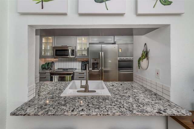 kitchen featuring appliances with stainless steel finishes, sink, backsplash, light stone counters, and kitchen peninsula