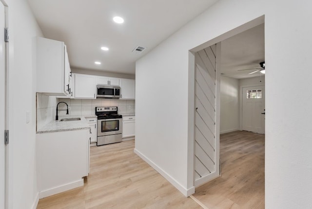 kitchen with sink, white cabinets, decorative backsplash, stainless steel appliances, and light hardwood / wood-style flooring