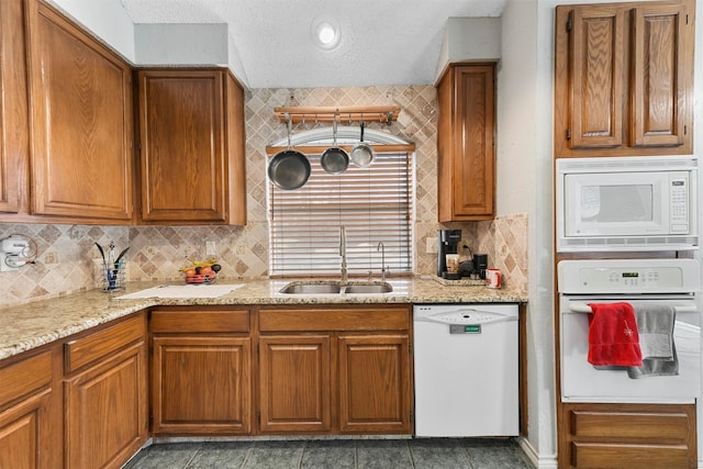 kitchen featuring light stone countertops, decorative backsplash, a textured ceiling, white appliances, and sink