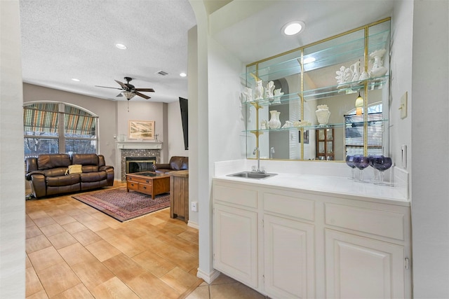 bar featuring white cabinets, a textured ceiling, ceiling fan, and sink