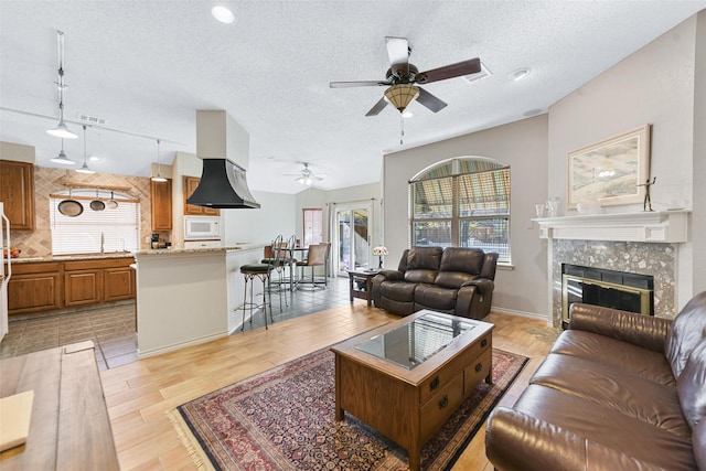 living room featuring a tile fireplace, sink, ceiling fan, a textured ceiling, and light hardwood / wood-style floors