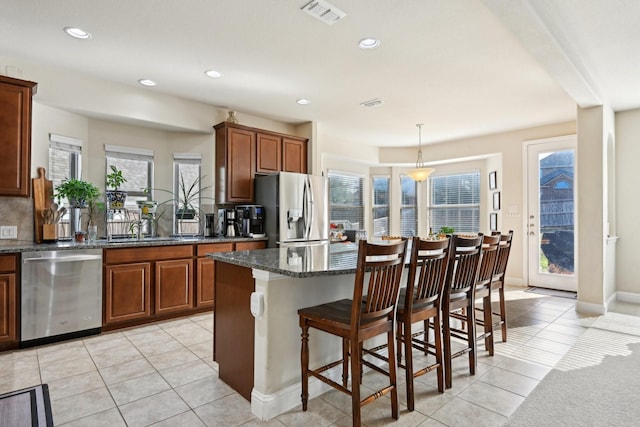 kitchen with hanging light fixtures, stainless steel appliances, light tile patterned floors, dark stone countertops, and a kitchen island