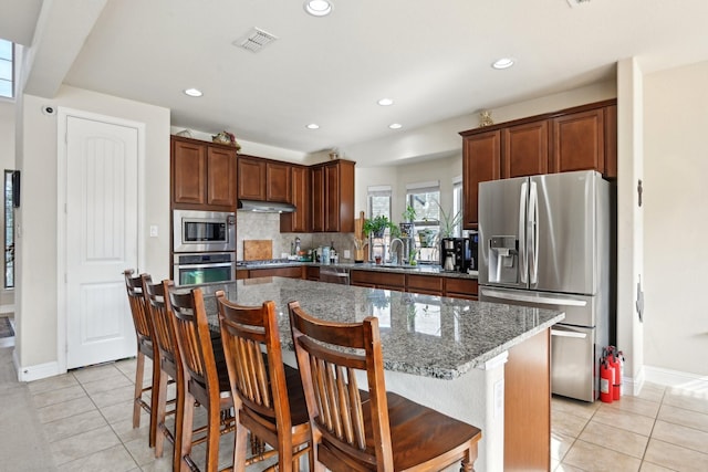 kitchen with a kitchen breakfast bar, a center island, light tile patterned floors, and appliances with stainless steel finishes