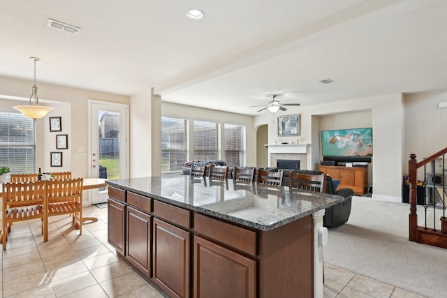 kitchen featuring ceiling fan, a center island, hanging light fixtures, dark stone countertops, and light tile patterned floors