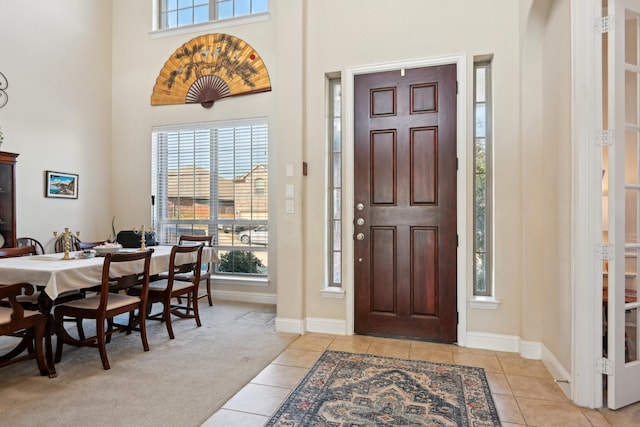 foyer entrance featuring light carpet, a towering ceiling, and a healthy amount of sunlight