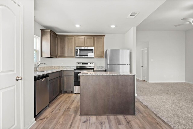 kitchen featuring ceiling fan, sink, a center island, stainless steel appliances, and light carpet