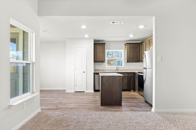 kitchen with sink, a center island, light colored carpet, dark brown cabinets, and appliances with stainless steel finishes