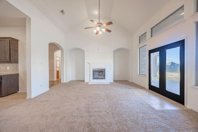 unfurnished living room with light carpet, french doors, high vaulted ceiling, and ceiling fan