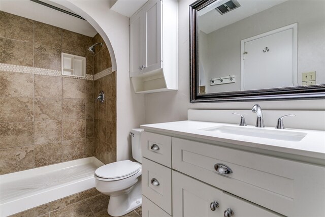 bathroom with a tile shower, vanity, and toilet