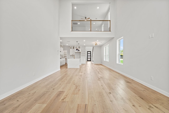 unfurnished living room with ceiling fan, sink, a high ceiling, and light wood-type flooring