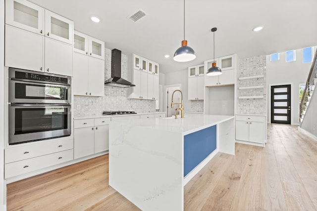 kitchen with wall chimney exhaust hood, white cabinetry, a kitchen island with sink, and stainless steel appliances