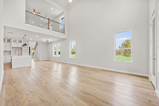 unfurnished living room with beamed ceiling, ceiling fan, light wood-type flooring, and a high ceiling