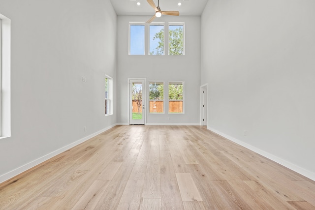 unfurnished living room featuring plenty of natural light, ceiling fan, light hardwood / wood-style floors, and a high ceiling