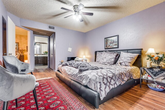 bedroom featuring a textured ceiling, hardwood / wood-style flooring, ensuite bath, and ceiling fan