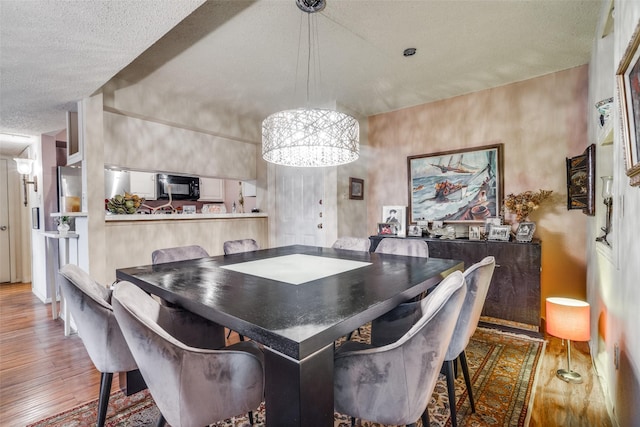 dining area featuring wood-type flooring, a textured ceiling, and an inviting chandelier