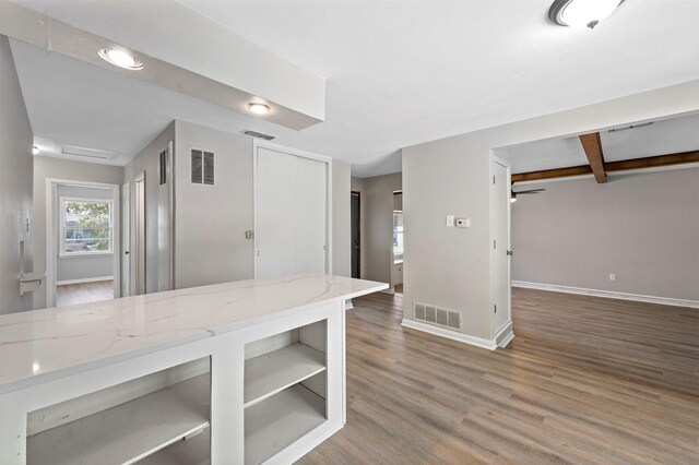 kitchen with beamed ceiling, wood-type flooring, and light stone countertops