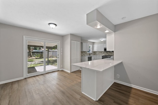 kitchen with wood-type flooring, kitchen peninsula, tasteful backsplash, white cabinetry, and stainless steel appliances