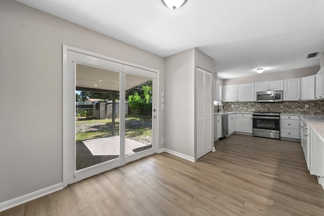 kitchen with backsplash, stainless steel appliances, white cabinetry, and light hardwood / wood-style flooring