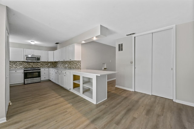 kitchen with tasteful backsplash, kitchen peninsula, appliances with stainless steel finishes, white cabinets, and light wood-type flooring