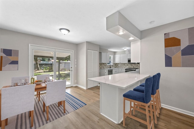 kitchen with white cabinetry, stainless steel appliances, kitchen peninsula, decorative backsplash, and light wood-type flooring