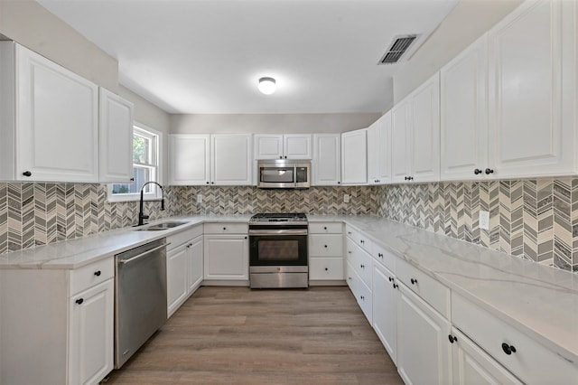 kitchen with white cabinetry, sink, light stone counters, appliances with stainless steel finishes, and light wood-type flooring