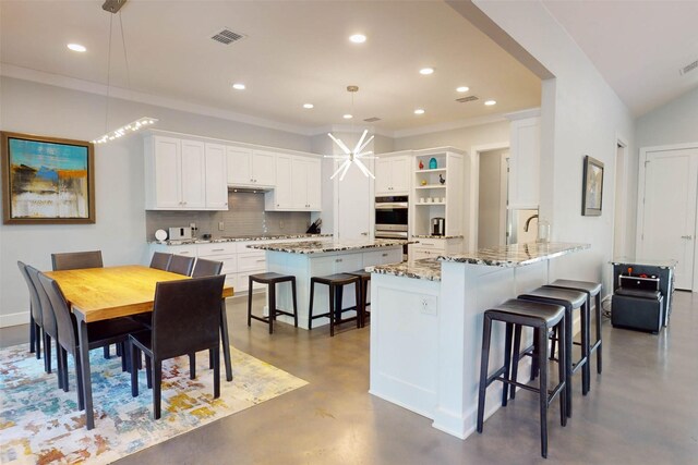 kitchen featuring a breakfast bar area, kitchen peninsula, white cabinets, and hanging light fixtures