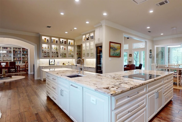 kitchen with black electric stovetop, sink, a large island, light stone counters, and white cabinetry