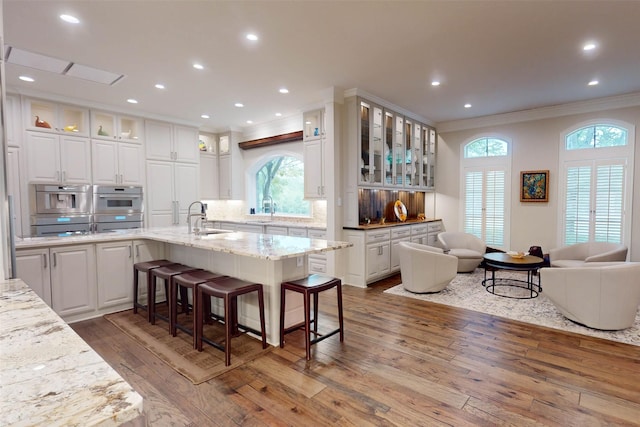 kitchen with white cabinets, light stone counters, a kitchen bar, and sink