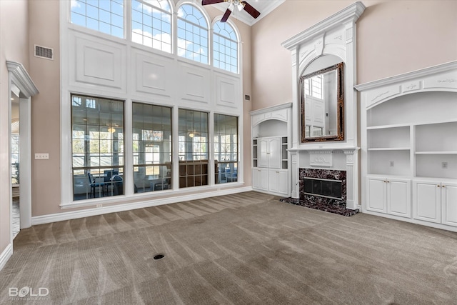 unfurnished living room with carpet flooring, built in shelves, ceiling fan, a high ceiling, and a premium fireplace