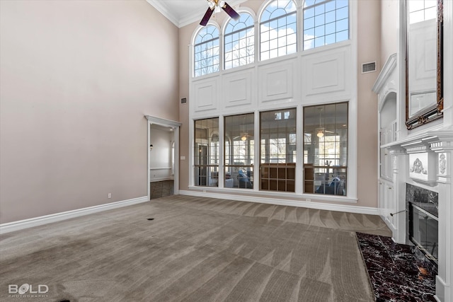 unfurnished living room with carpet, ornamental molding, ceiling fan, a fireplace, and a high ceiling