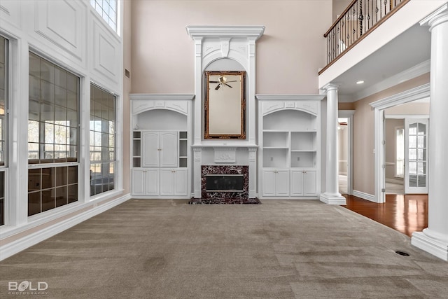 unfurnished living room featuring a high end fireplace, built in features, ornate columns, and a towering ceiling