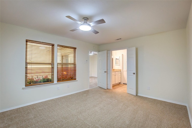 unfurnished bedroom with ceiling fan, light colored carpet, and ensuite bath