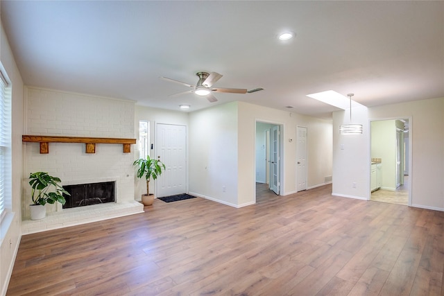 unfurnished living room with a skylight, ceiling fan, a fireplace, and hardwood / wood-style flooring