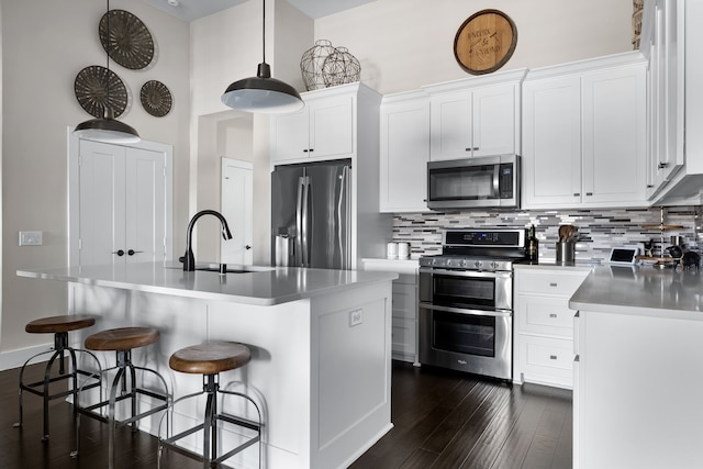 kitchen with appliances with stainless steel finishes, white cabinets, dark hardwood / wood-style flooring, backsplash, and a kitchen island with sink