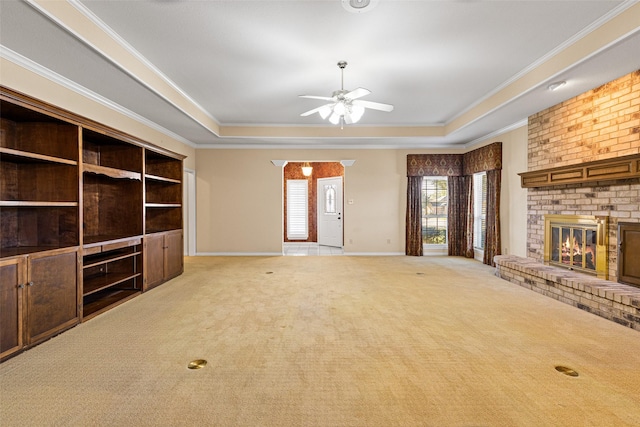 unfurnished living room with ceiling fan, ornamental molding, a fireplace, a tray ceiling, and light colored carpet