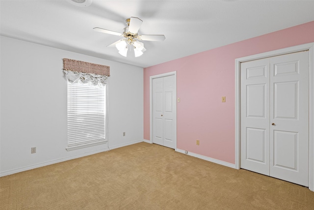 unfurnished bedroom with ceiling fan, light carpet, and multiple closets