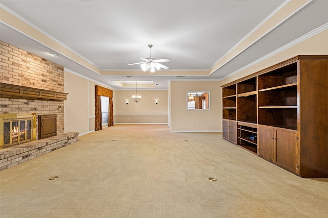 unfurnished living room with a brick fireplace, ornamental molding, ceiling fan with notable chandelier, a tray ceiling, and light colored carpet