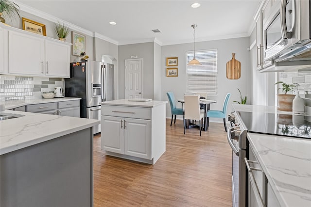 kitchen featuring decorative backsplash, appliances with stainless steel finishes, pendant lighting, white cabinetry, and a kitchen island