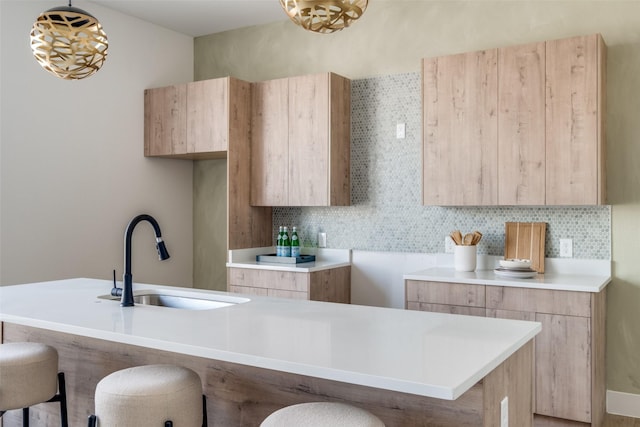 kitchen with a breakfast bar, sink, backsplash, decorative light fixtures, and light brown cabinetry