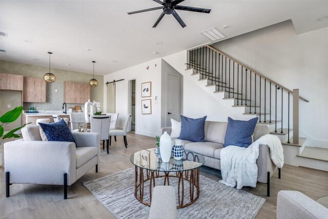 living room featuring a barn door, ceiling fan, sink, and light wood-type flooring