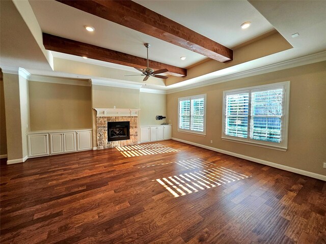 unfurnished living room with beam ceiling, ceiling fan, a stone fireplace, dark hardwood / wood-style floors, and crown molding