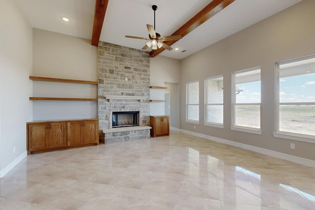 unfurnished living room with beamed ceiling, ceiling fan, a stone fireplace, and baseboards