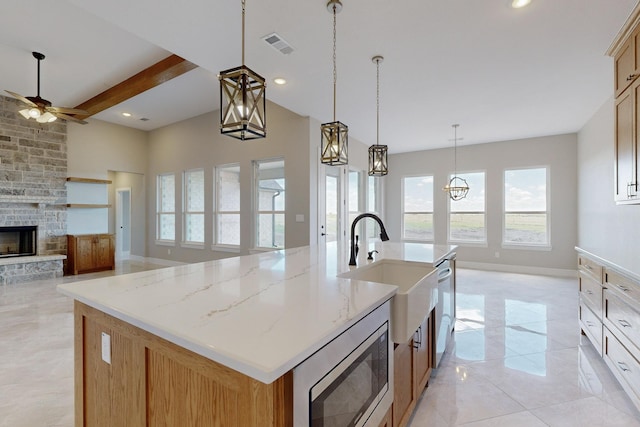 kitchen with a fireplace, beam ceiling, built in microwave, and an island with sink