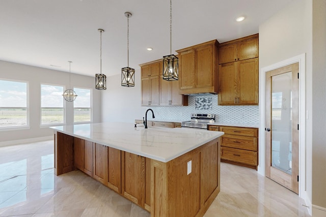 kitchen featuring light stone counters, a center island with sink, hanging light fixtures, stainless steel range with electric stovetop, and tasteful backsplash