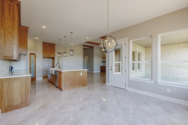 kitchen featuring a center island with sink, light countertops, an inviting chandelier, brown cabinetry, and stainless steel dishwasher