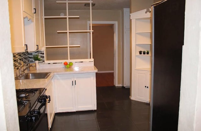 kitchen featuring backsplash, black range with gas stovetop, sink, dark tile patterned flooring, and white cabinets